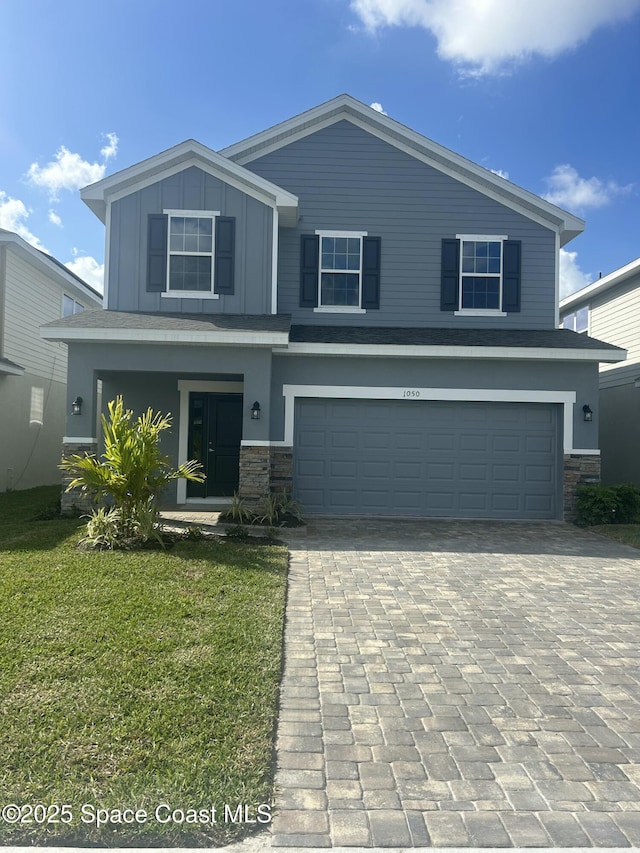 view of front facade with board and batten siding, a front lawn, decorative driveway, stone siding, and an attached garage