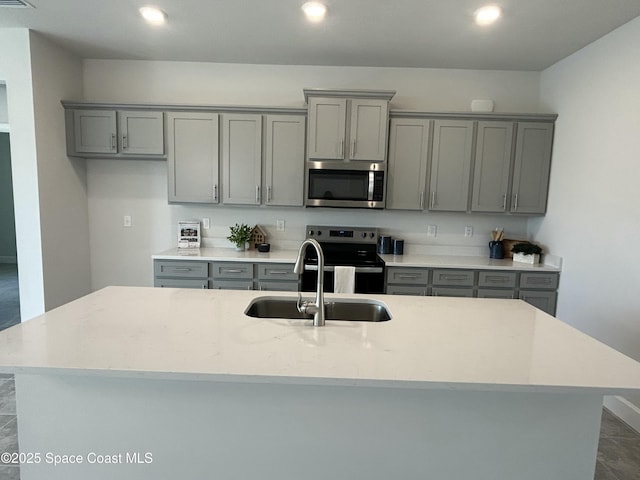 kitchen with an island with sink, recessed lighting, gray cabinets, stainless steel appliances, and a sink