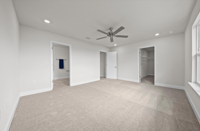 unfurnished bedroom with a spacious closet, a closet, ceiling fan, and light colored carpet