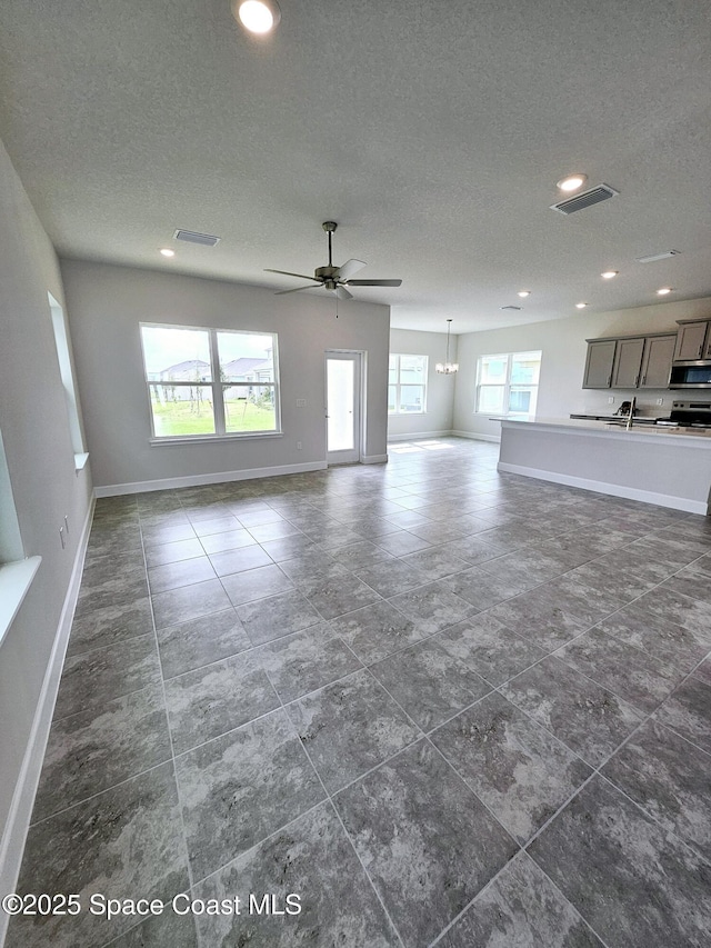 unfurnished living room featuring ceiling fan with notable chandelier, sink, and a textured ceiling