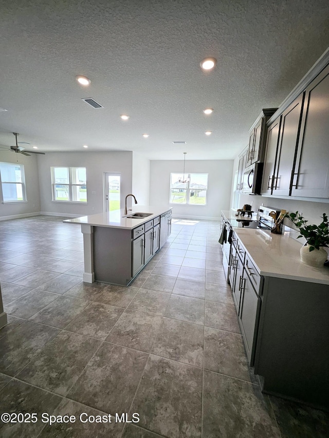 kitchen featuring electric stove, sink, a kitchen island with sink, and a healthy amount of sunlight