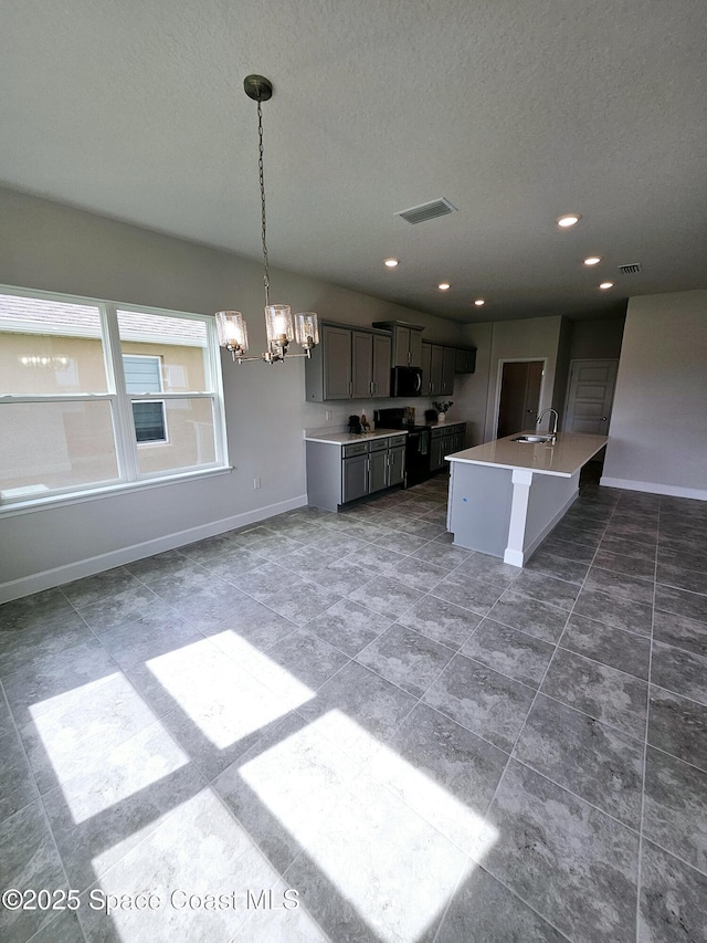 kitchen with a center island with sink, gray cabinetry, sink, a chandelier, and pendant lighting