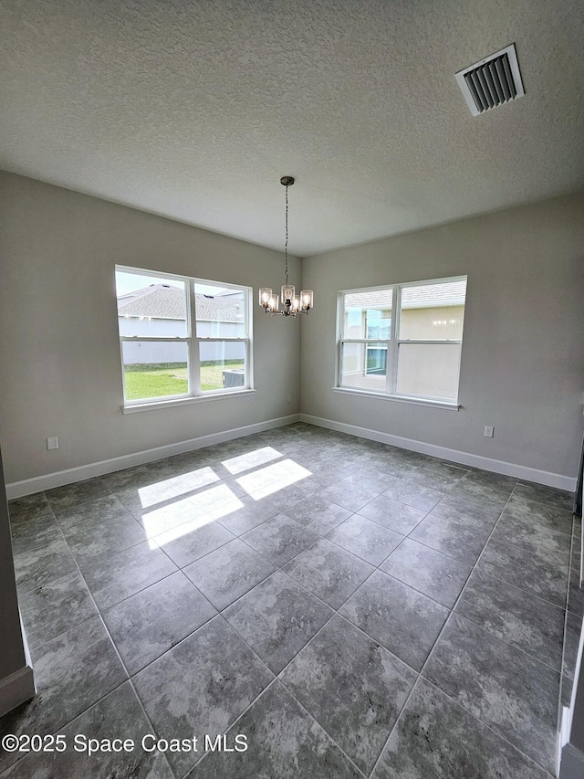 tiled spare room featuring plenty of natural light, an inviting chandelier, and a textured ceiling