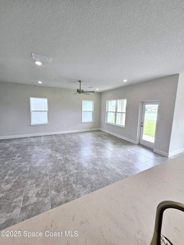 empty room featuring ceiling fan, tile patterned flooring, a textured ceiling, and plenty of natural light