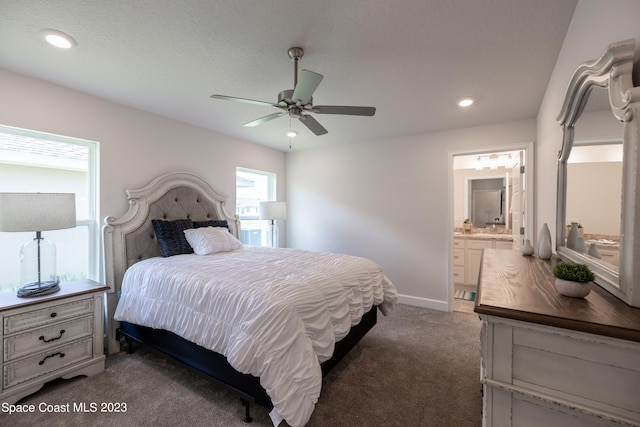 bedroom with a textured ceiling, ensuite bathroom, dark carpet, and ceiling fan