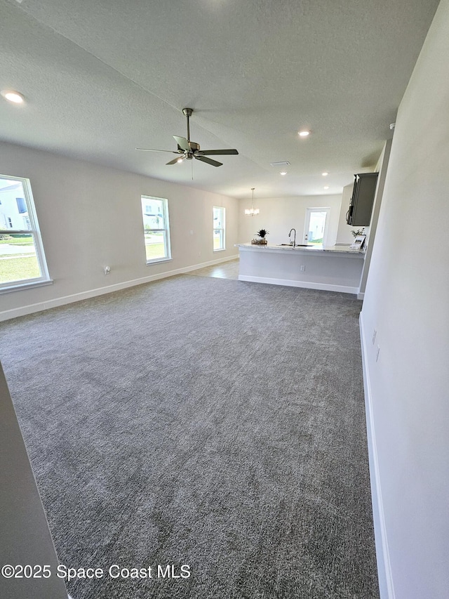 unfurnished living room with dark carpet, a wealth of natural light, and a textured ceiling