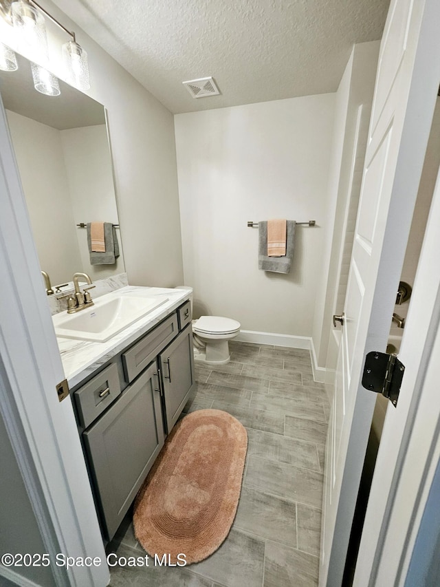 bathroom with vanity, a textured ceiling, a bathing tub, and toilet