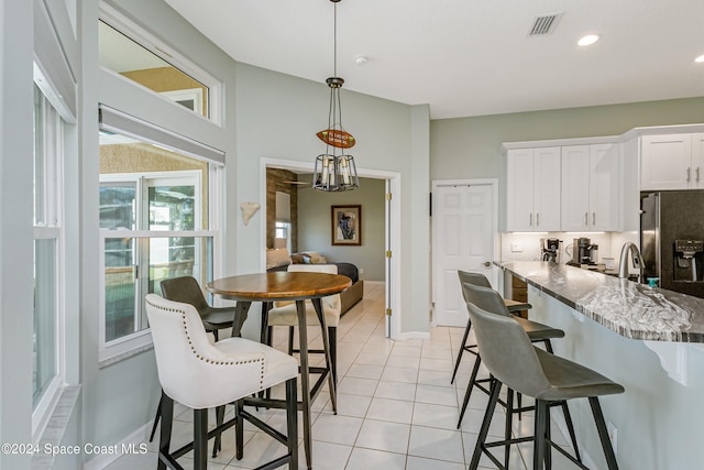 kitchen with a kitchen bar, stainless steel fridge, white cabinetry, decorative light fixtures, and light stone counters