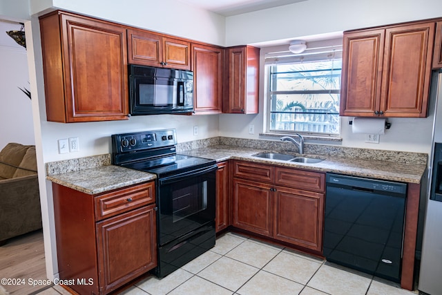 kitchen with sink, light tile patterned floors, black appliances, and light stone countertops