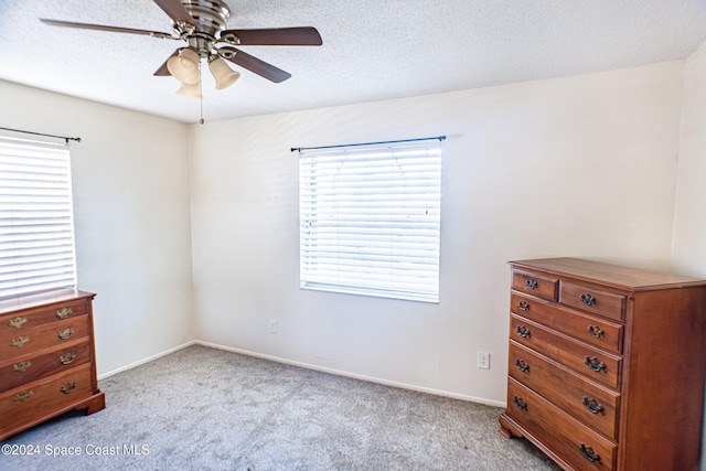 bedroom with ceiling fan, light carpet, multiple windows, and a textured ceiling