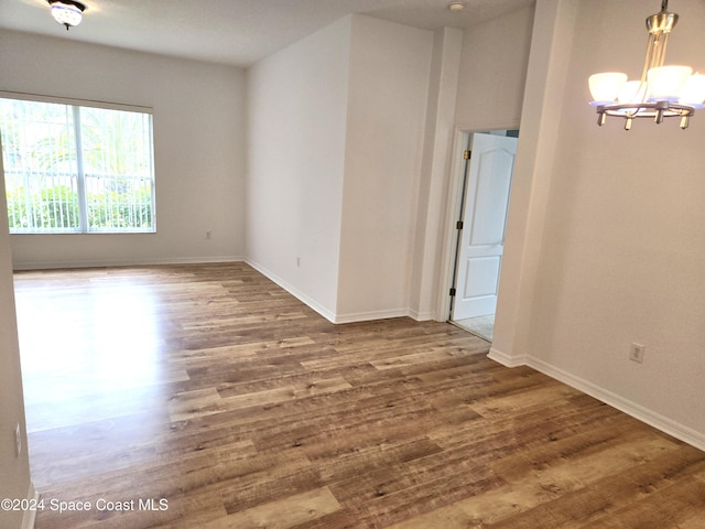 empty room with wood-type flooring and an inviting chandelier