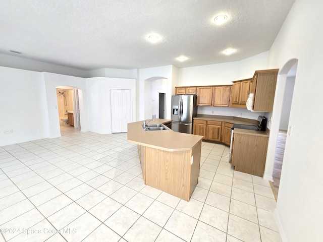 kitchen with a textured ceiling, a kitchen island with sink, range, stainless steel refrigerator with ice dispenser, and sink