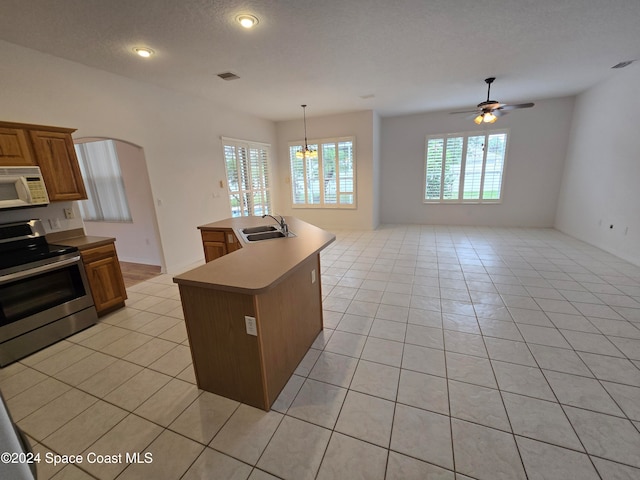 kitchen with hanging light fixtures, electric range, light tile patterned floors, an island with sink, and ceiling fan with notable chandelier