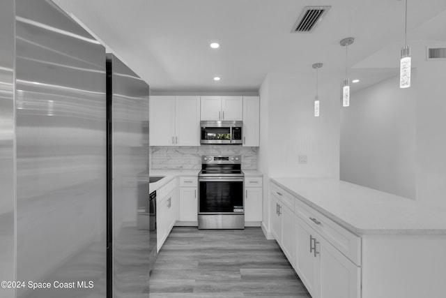 kitchen with appliances with stainless steel finishes, light wood-type flooring, kitchen peninsula, white cabinetry, and pendant lighting