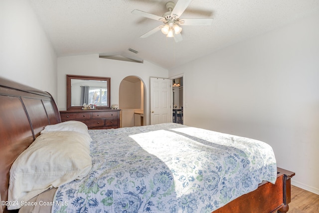 bedroom with lofted ceiling, a textured ceiling, light hardwood / wood-style floors, and ceiling fan