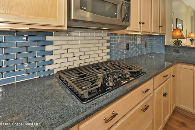 kitchen with tasteful backsplash, black gas stovetop, light brown cabinetry, and dark stone counters