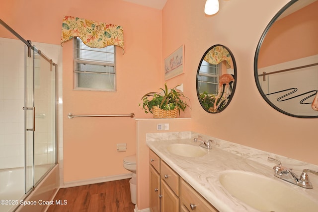 full bathroom with combined bath / shower with glass door, vanity, hardwood / wood-style flooring, and toilet