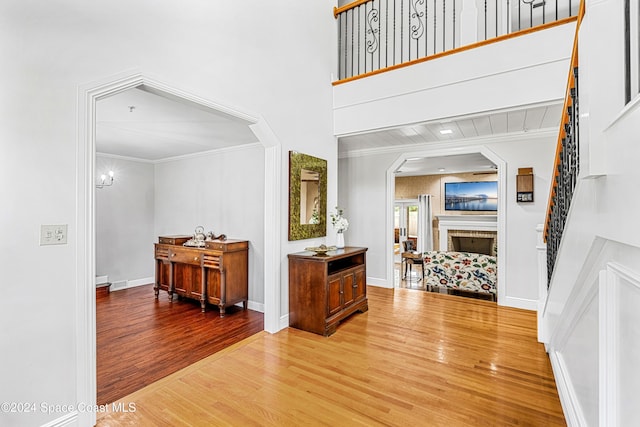 entryway with crown molding, a fireplace, wood-type flooring, and a towering ceiling