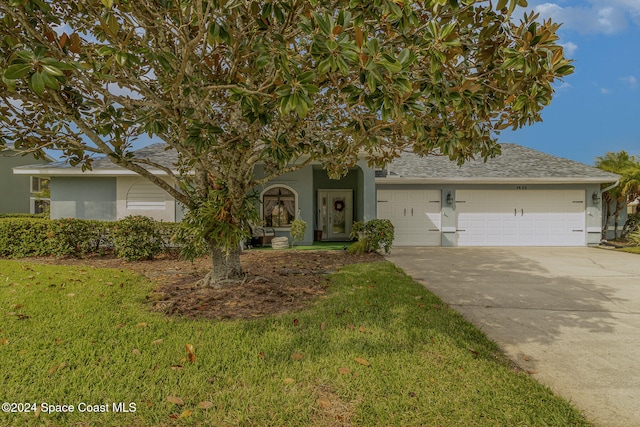 view of property hidden behind natural elements featuring a garage and a front yard