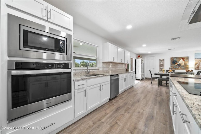 kitchen featuring white cabinets, sink, light wood-type flooring, light stone counters, and stainless steel appliances