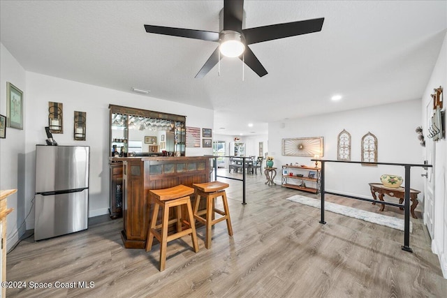 kitchen with a kitchen breakfast bar, stainless steel fridge, ceiling fan, and light hardwood / wood-style flooring