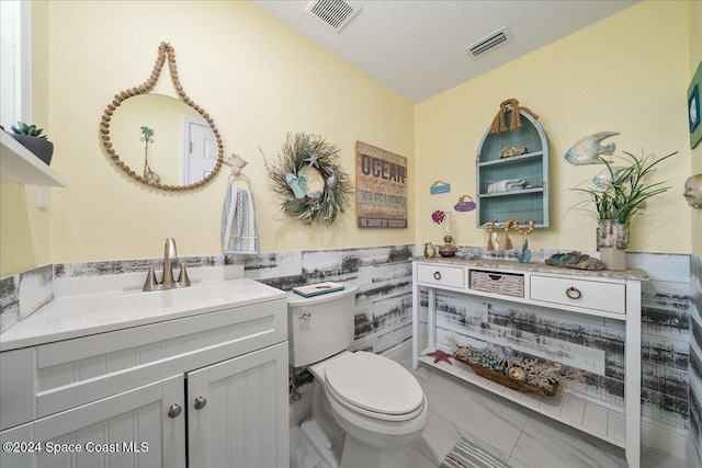 bathroom with tile patterned flooring, a textured ceiling, toilet, vanity, and tile walls