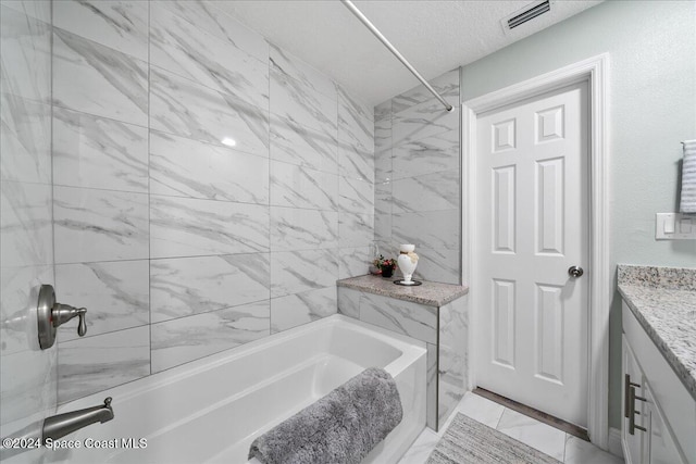 bathroom with vanity, a textured ceiling, and tiled shower / bath combo