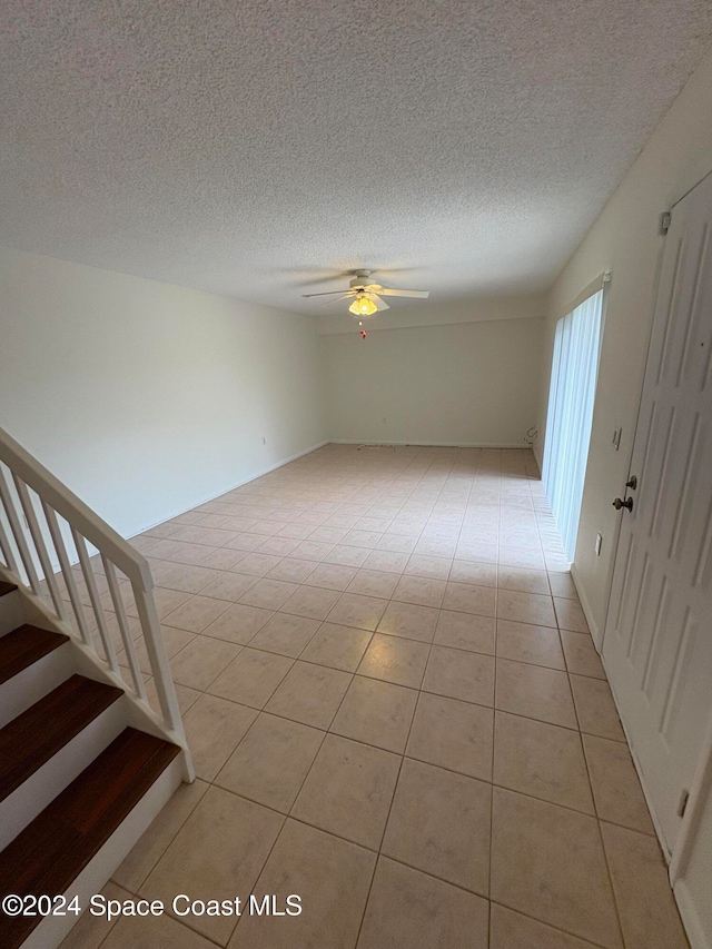 spare room featuring a textured ceiling, light tile patterned floors, and ceiling fan