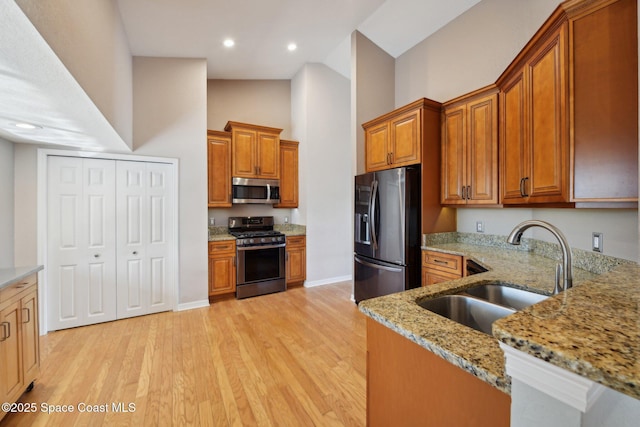 kitchen with sink, a towering ceiling, appliances with stainless steel finishes, light hardwood / wood-style floors, and light stone counters