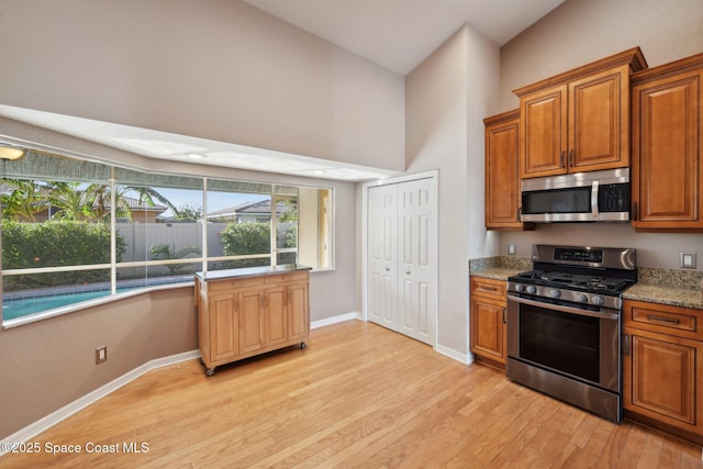 kitchen with light stone countertops, light wood-type flooring, stainless steel appliances, and vaulted ceiling