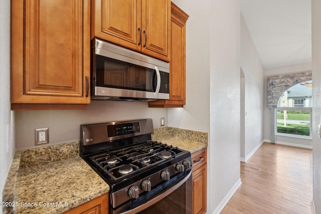 kitchen featuring light wood-type flooring, stainless steel appliances, light stone counters, and vaulted ceiling