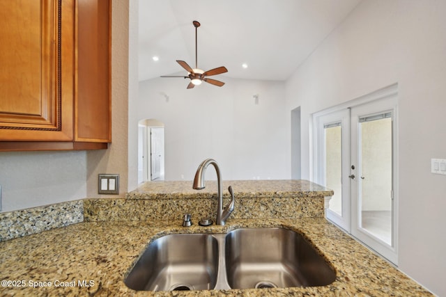 kitchen with ceiling fan, french doors, sink, light stone counters, and vaulted ceiling