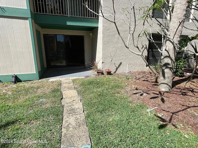 view of exterior entry featuring a lawn and a balcony