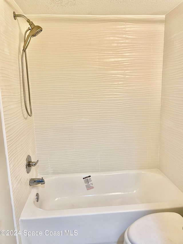 bathroom with tiled shower / bath, a textured ceiling, and toilet