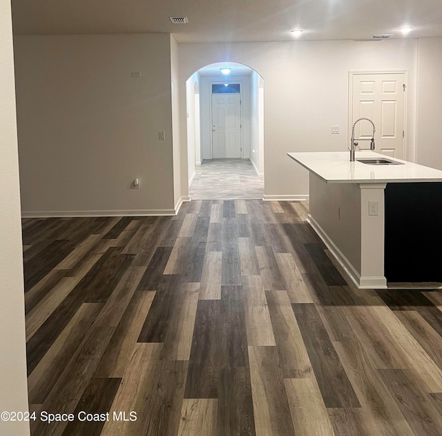 kitchen with a center island with sink, sink, and dark wood-type flooring