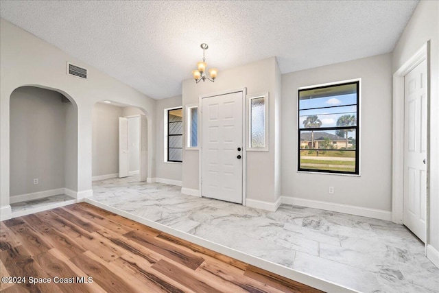 foyer with lofted ceiling, a textured ceiling, hardwood / wood-style flooring, and a chandelier