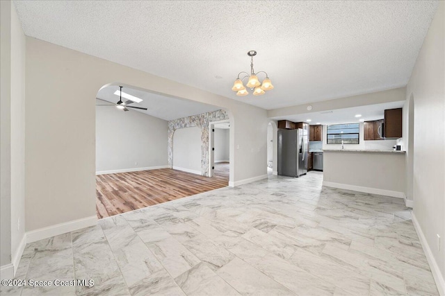 unfurnished living room with a textured ceiling, ceiling fan with notable chandelier, and light wood-type flooring