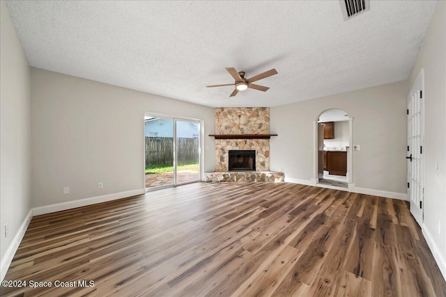 unfurnished living room featuring ceiling fan, a stone fireplace, a textured ceiling, and dark hardwood / wood-style flooring