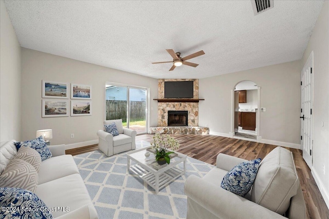 living room featuring a stone fireplace, hardwood / wood-style floors, a textured ceiling, and ceiling fan