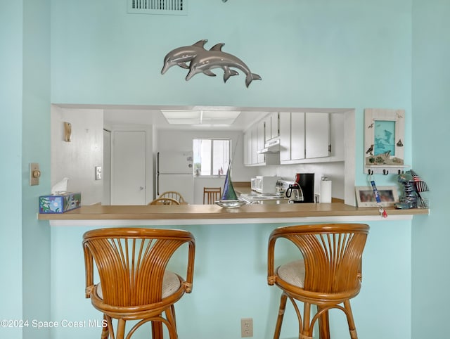 kitchen with a breakfast bar, white cabinetry, kitchen peninsula, and white appliances