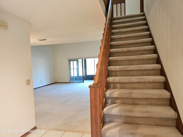 stairway with carpet floors and a textured ceiling