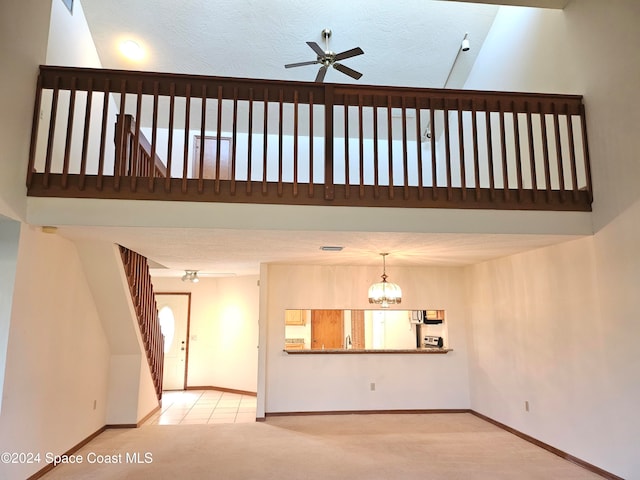 unfurnished living room featuring a towering ceiling, a textured ceiling, light carpet, and ceiling fan with notable chandelier