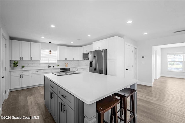 kitchen with hanging light fixtures, wood-type flooring, white cabinets, gray cabinets, and appliances with stainless steel finishes