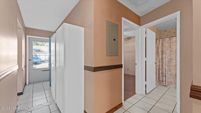 corridor with electric panel, a textured ceiling, and light tile patterned floors