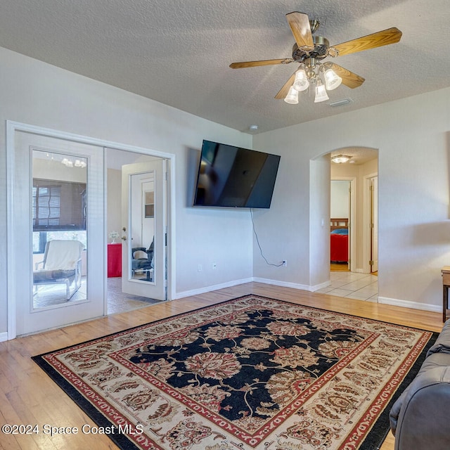 living room with french doors, a textured ceiling, light wood-type flooring, and ceiling fan