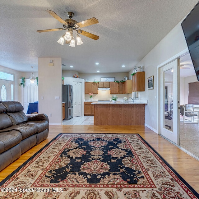 living room with ceiling fan, light hardwood / wood-style floors, and a textured ceiling