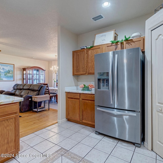 kitchen featuring a textured ceiling, light tile patterned flooring, stainless steel refrigerator with ice dispenser, and a notable chandelier