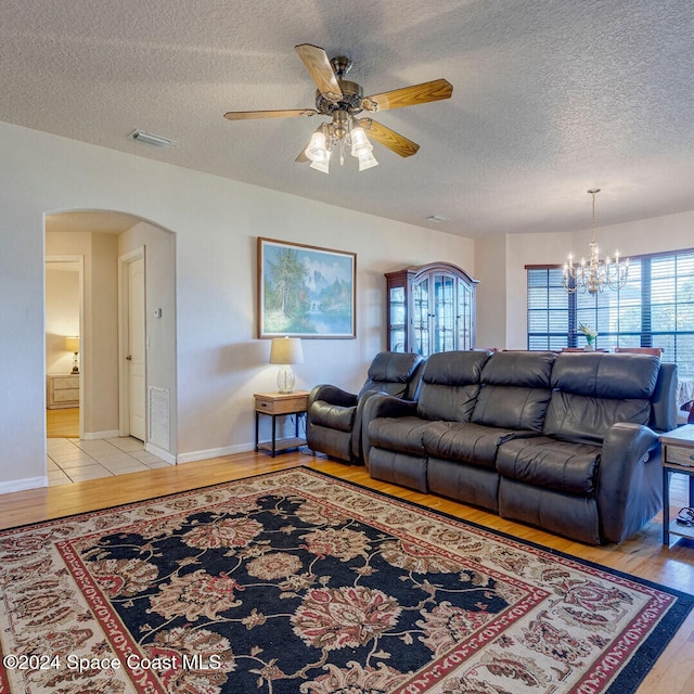 living room featuring ceiling fan with notable chandelier, a textured ceiling, and light wood-type flooring