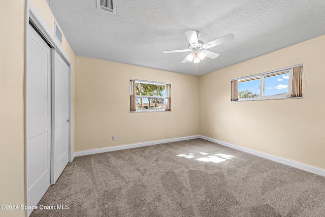 unfurnished bedroom featuring ceiling fan, a closet, a textured ceiling, and carpet flooring