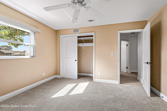 unfurnished bedroom featuring ceiling fan, a closet, light carpet, and a textured ceiling